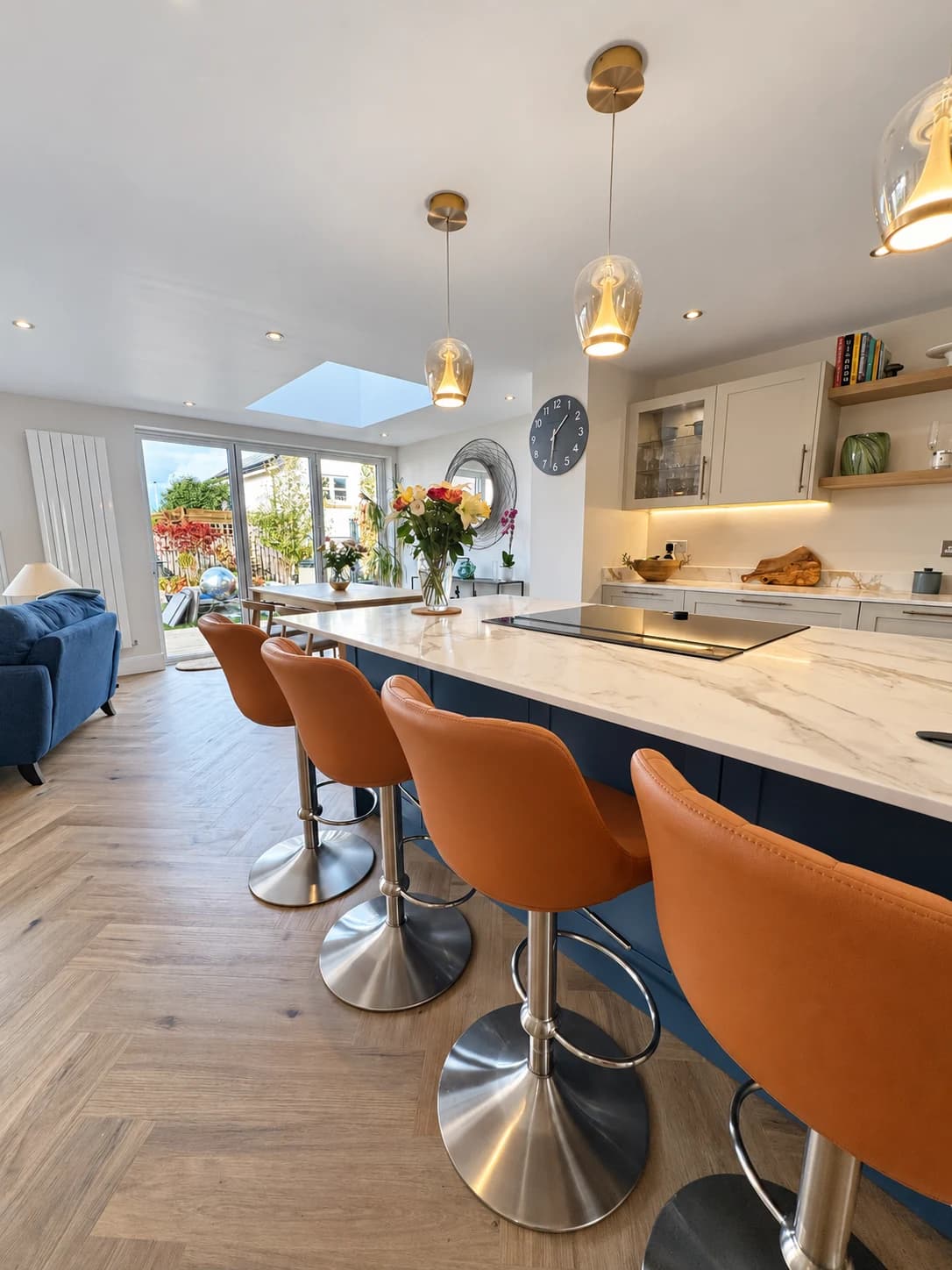 Open-plan kitchen with a pale island worktop, blue cabinetry, orange bar stools and garden-facing doors